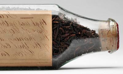 Glass bottle full of dry tea leaves positioned on its side so the handwritten label is visible